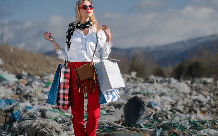 Jeune femme portant des sacs de shopping au milieu d'une décharge de textiles